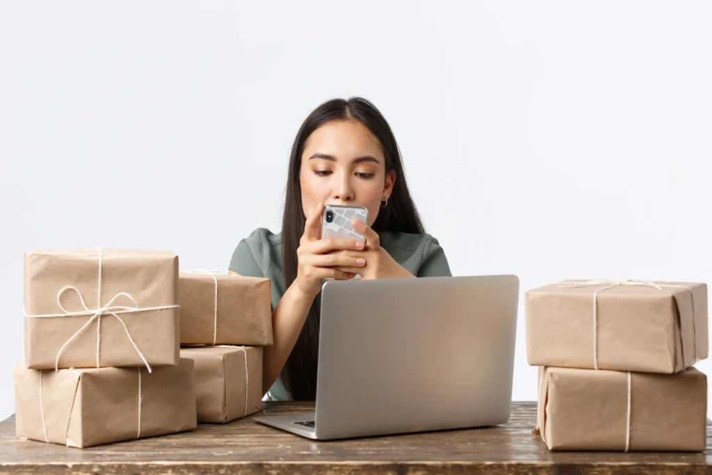 Mujer escribiendo en su celular rodeada por cajas que pertenecen a un ecommerce