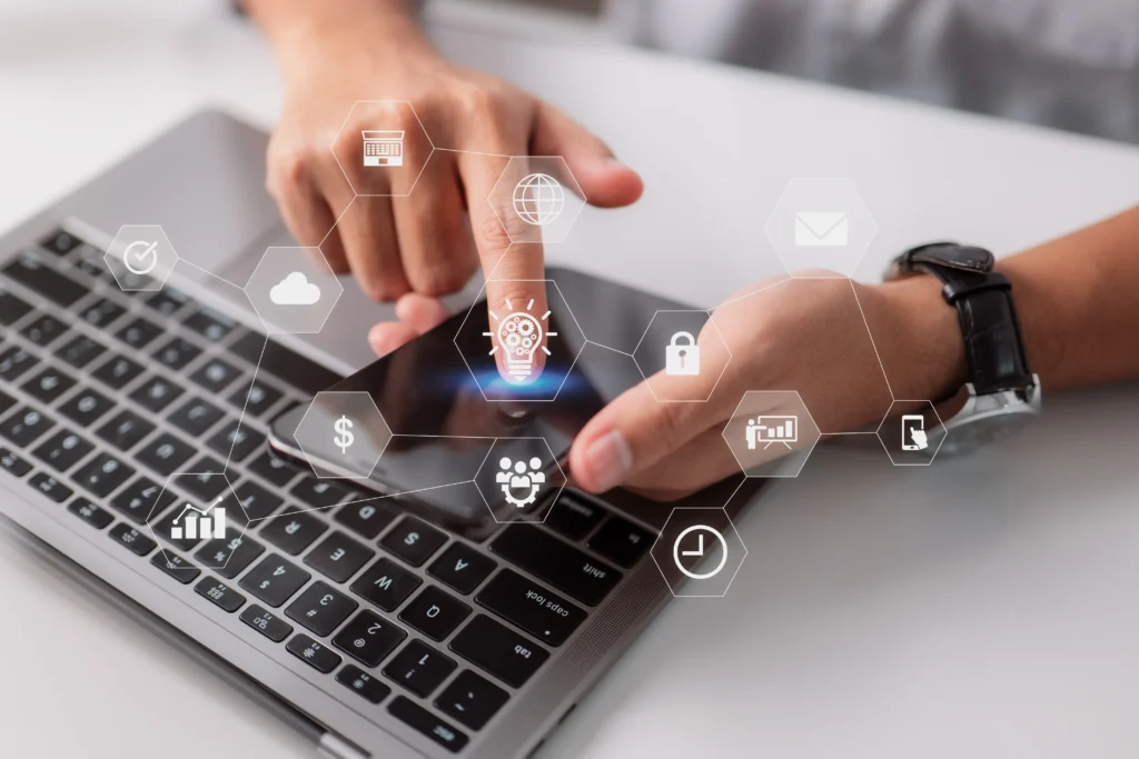 Mano usando smartphone sobre teclado de laptop con iconos de servicios digitales y ciberseguridad