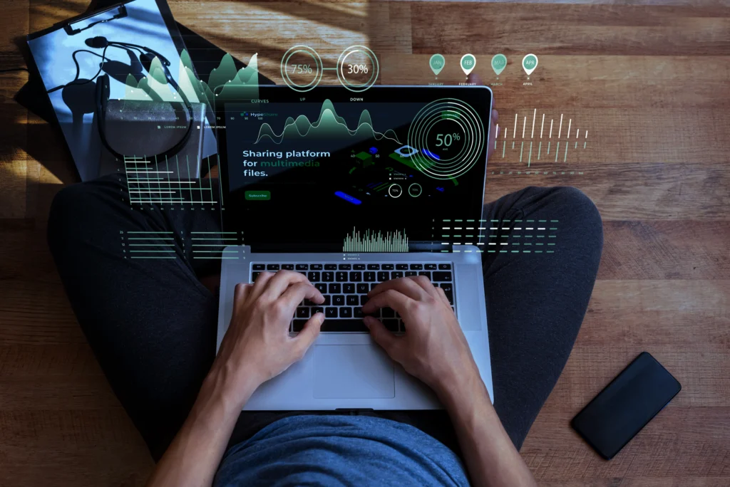 Persona escribiendo en un computador portátil abierto y se muestran datos flotantes